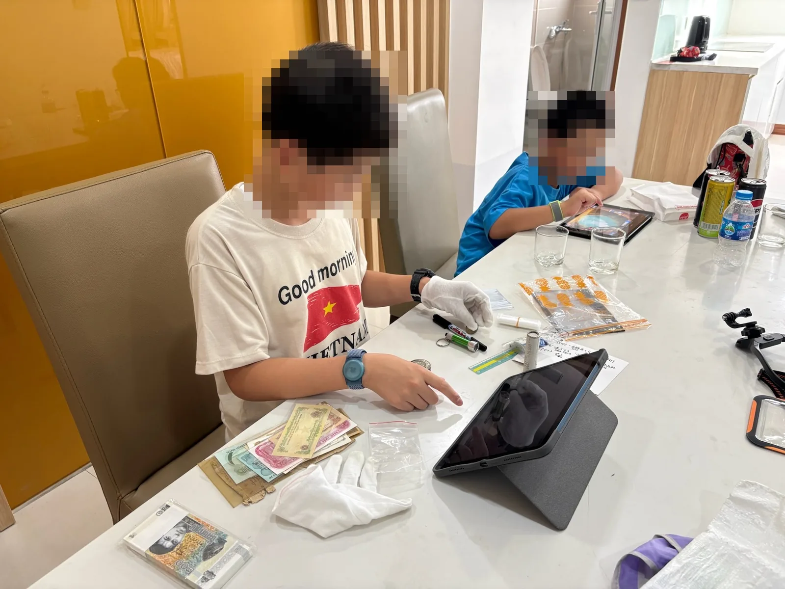 ホテルのテーブルで古銭と旧紙幣をタブレットで調べる子どもたち
